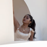 A model framed with a white wall and archway behind her, wearing a pink satin dress and silver jewelry. 
