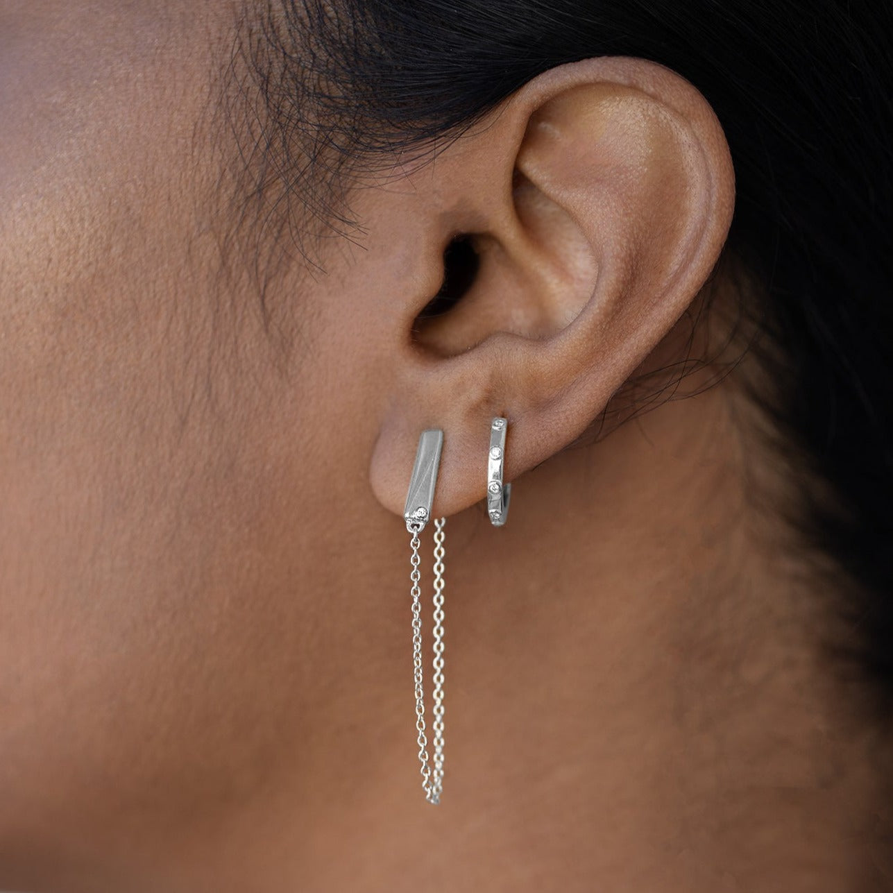 Flex falling chain earrings with lab grown diamonds close up on a model's ear with a hoop earring in the second piercing.