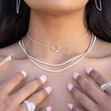 A close up of a model wearing sterling silver necklaces with her hands on her chest. 