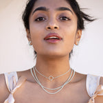 A model wearing three sterling silver chains and silver necklaces with pink bows around her shoulders. 