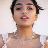 A model wearing three sterling silver chains and silver necklaces with pink bows around her shoulders. 