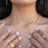 A close up of a model's neck with her hands on her chest adorned with gold necklaces and rings. 