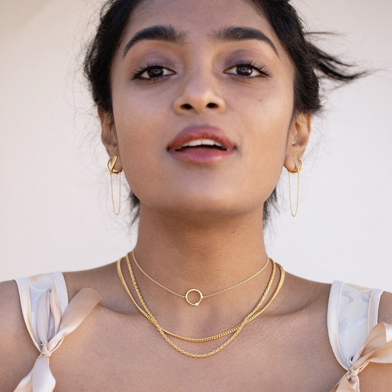 A close up of a model's face adorned with gold necklaces and gold earrings. 