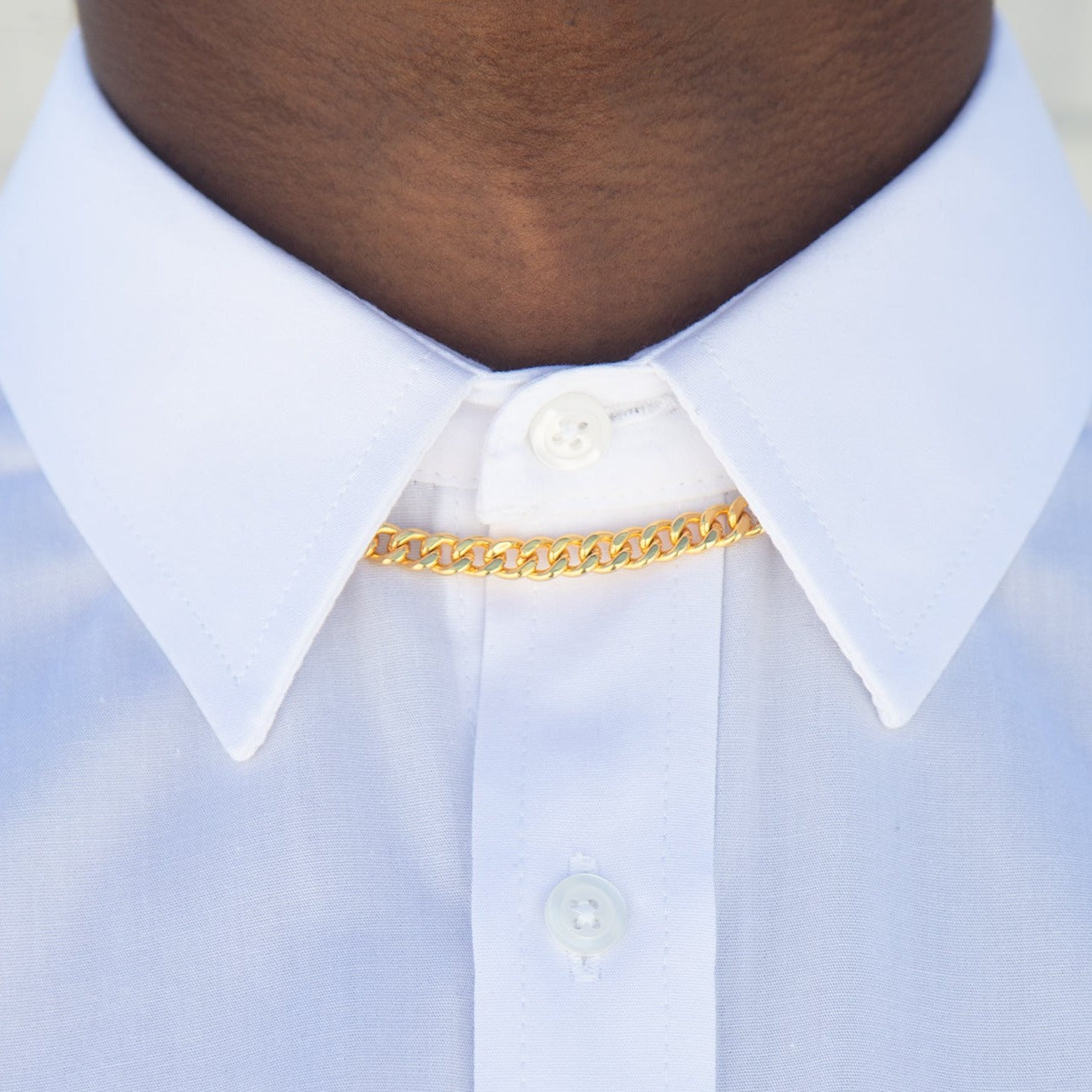 A cuban link chain under a white button up shirt collar, with soft lighting. 
