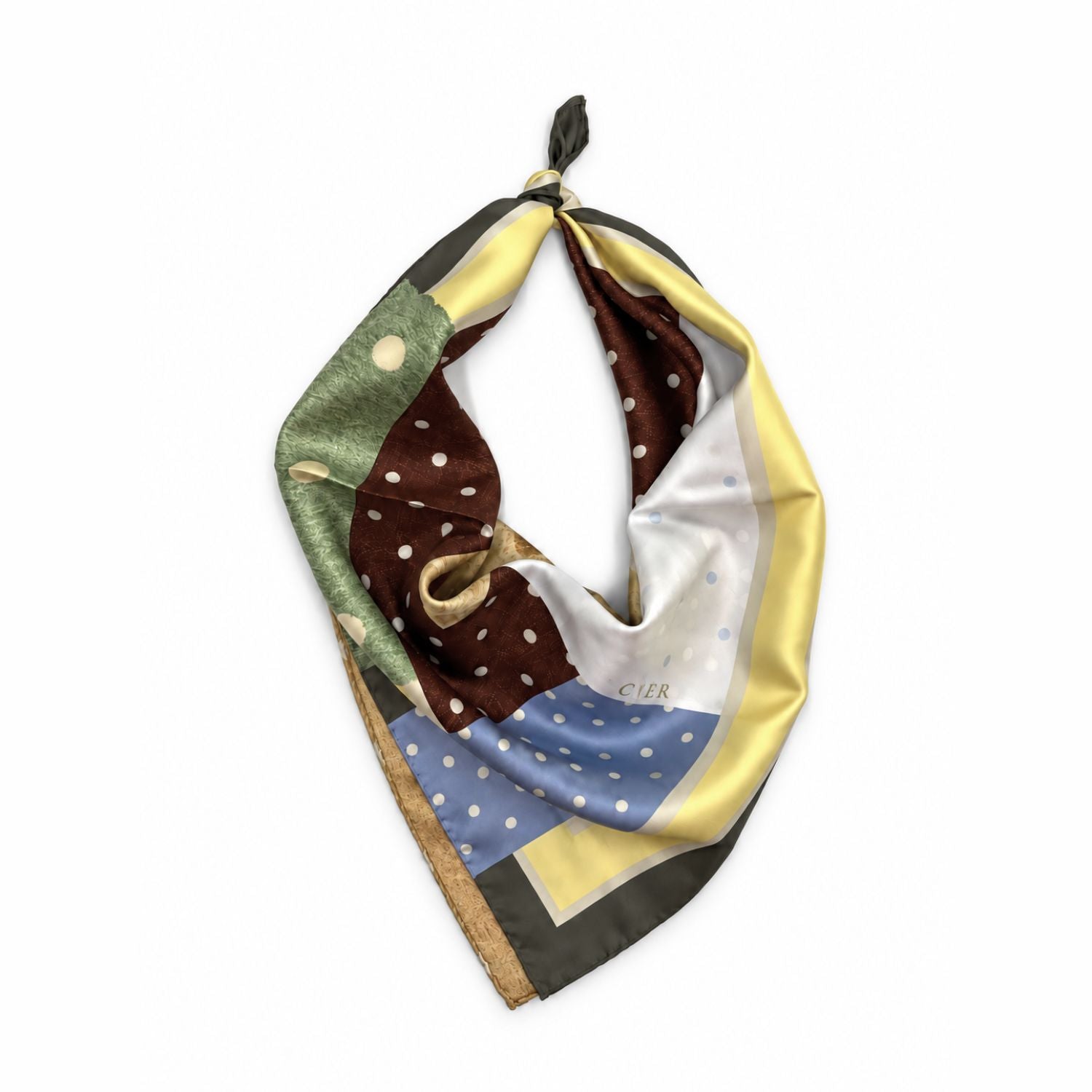 A square silk scarf with a multicolor patchwork print featuring brown polka dots, a blue polka dot section, olive green, white, and yellow panels, tied in a loop on a white background.