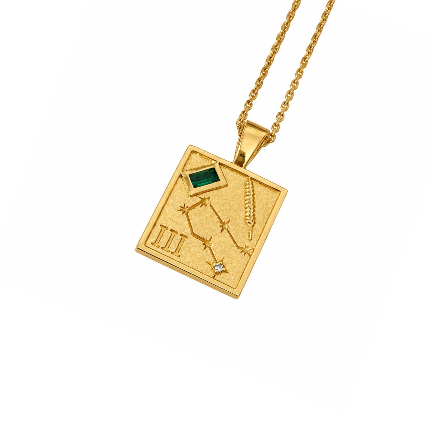A gold pendant necklace featuring a square celestial map design with Roman numerals, a constellation, a wheat stalk, and a small green rectangular stone, shown on a white background.