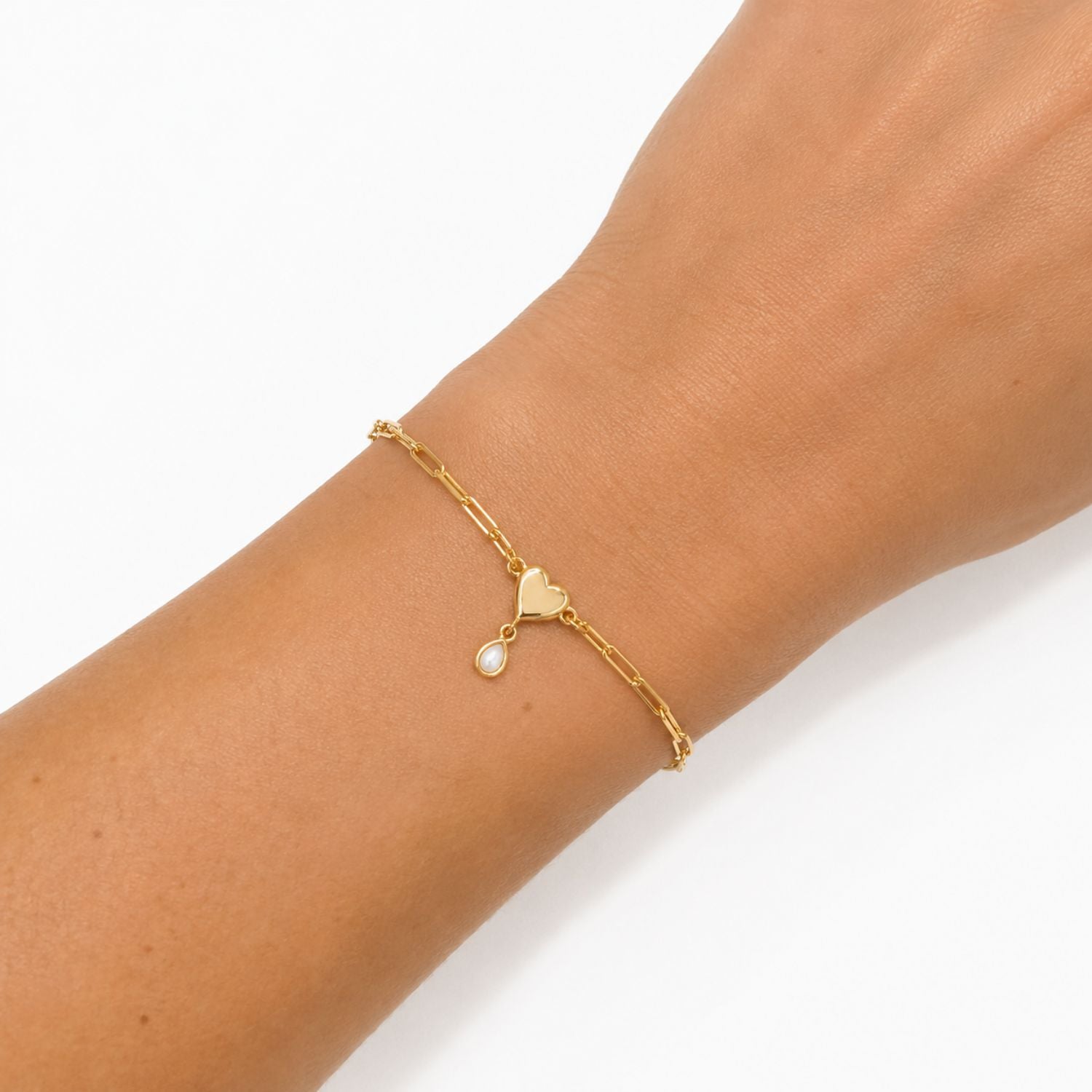 A delicate gold chain bracelet with a small heart charm and a teardrop pearl pendant, shown worn on a person's wrist against a clean white background.