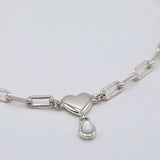 A silver paperclip chain necklace featuring a polished heart-shaped pendant and a small teardrop-shaped white pearl charm, shown on a clean light gray background.
