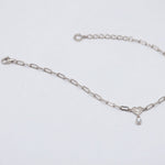 A silver paperclip chain bracelet with a small heart charm and teardrop pearl, displayed on a clean white background.