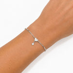 A delicate silver chain bracelet with a small heart and teardrop charm, shown worn on a person's wrist against a clean white background.