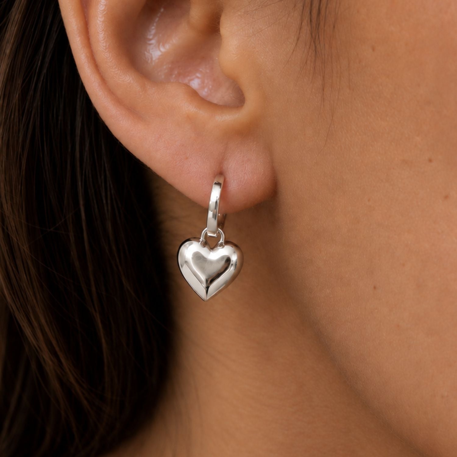 A close-up of a person's ear wearing a polished silver heart-shaped dangle earring.