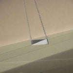 A silver necklace on a delicate chain with a green and grey background and reflection on the bottom of the image. 