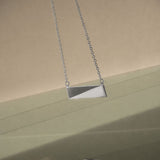 A silver necklace on a delicate chain with a green and grey background and reflection on the bottom of the image. 