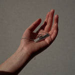 A sterling silver flex necklace and silver ring in the palm of an extended, hand  with a gray background. 