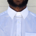 A man wearing a sterling silver rope chain under the collar of a white button up shirt with a white wall behind him. 