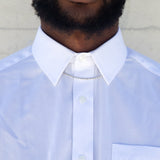 A man wearing a sterling silver rope chain under the collar of a white button up shirt with a white wall behind him. 