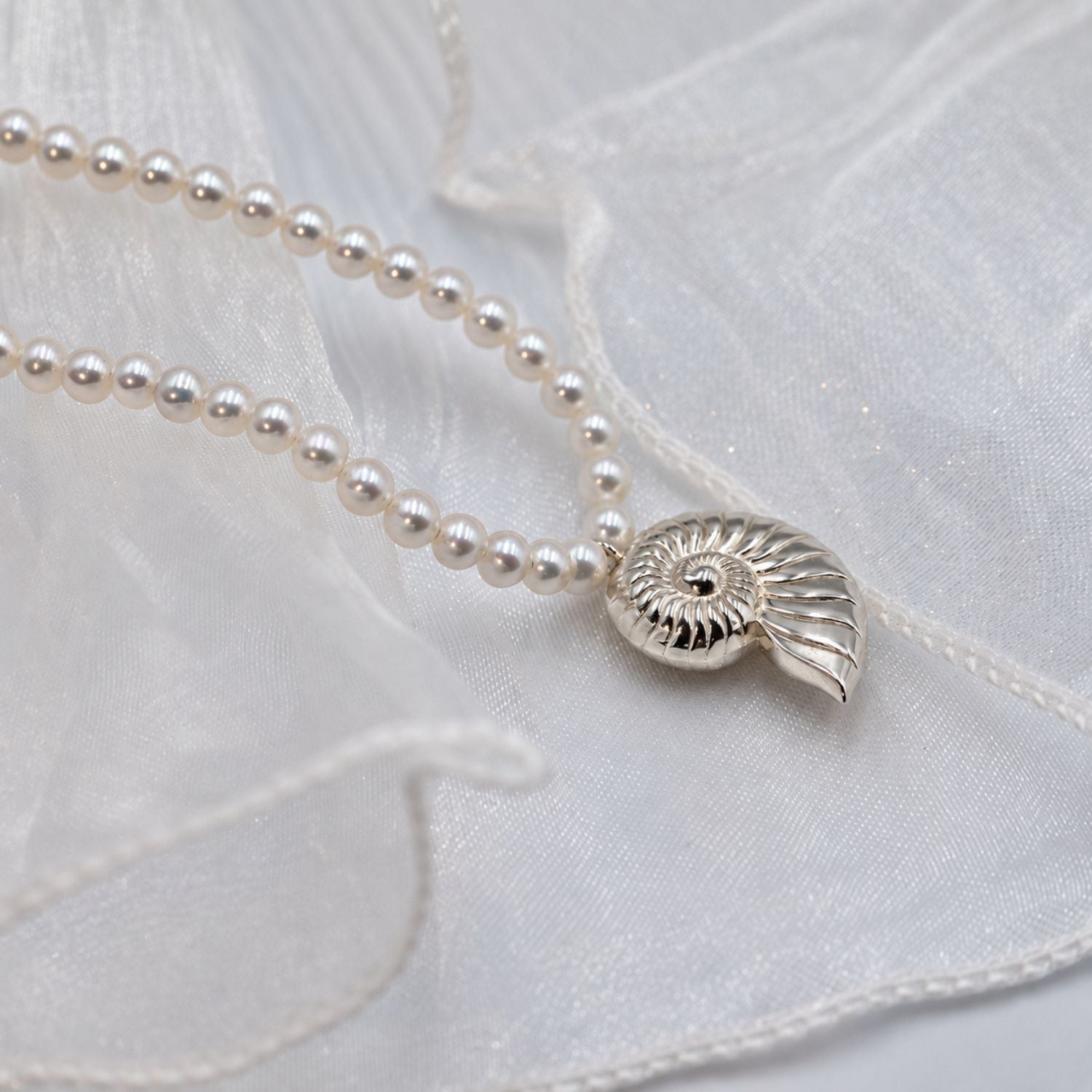 A delicate necklace with small white pearls and a gold shell-shaped pendant, laid on soft white fabric.