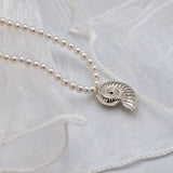 A delicate necklace with small white pearls and a gold shell-shaped pendant, laid on soft white fabric.