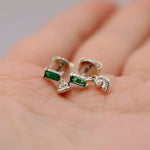 A pair of silver-toned earrings with rectangular green gemstones and small dangling spiral charms, resting on a person's palm.