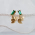 A pair of gold vermeil dangle earrings featuring rectangular green emerald-cut crystals on the studs and a matching gold nautilus shell charm hanging below, displayed against a soft white fabric background.