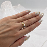 Ring with nautilus shell in 14K gold vermeil, blue sapphire, pearl and lab-grown diamond on a hand with a grey background with soft white fabric.