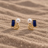 14K gold vermeil stud earrings with a blue sapphire, shell, lab-grown diamond and pearl on sand.