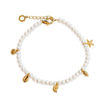 A delicate pearl bracelet with gold-toned metal charms, including a starfish, seashell, leaf, and a lobster clasp, displayed on a clean white background.