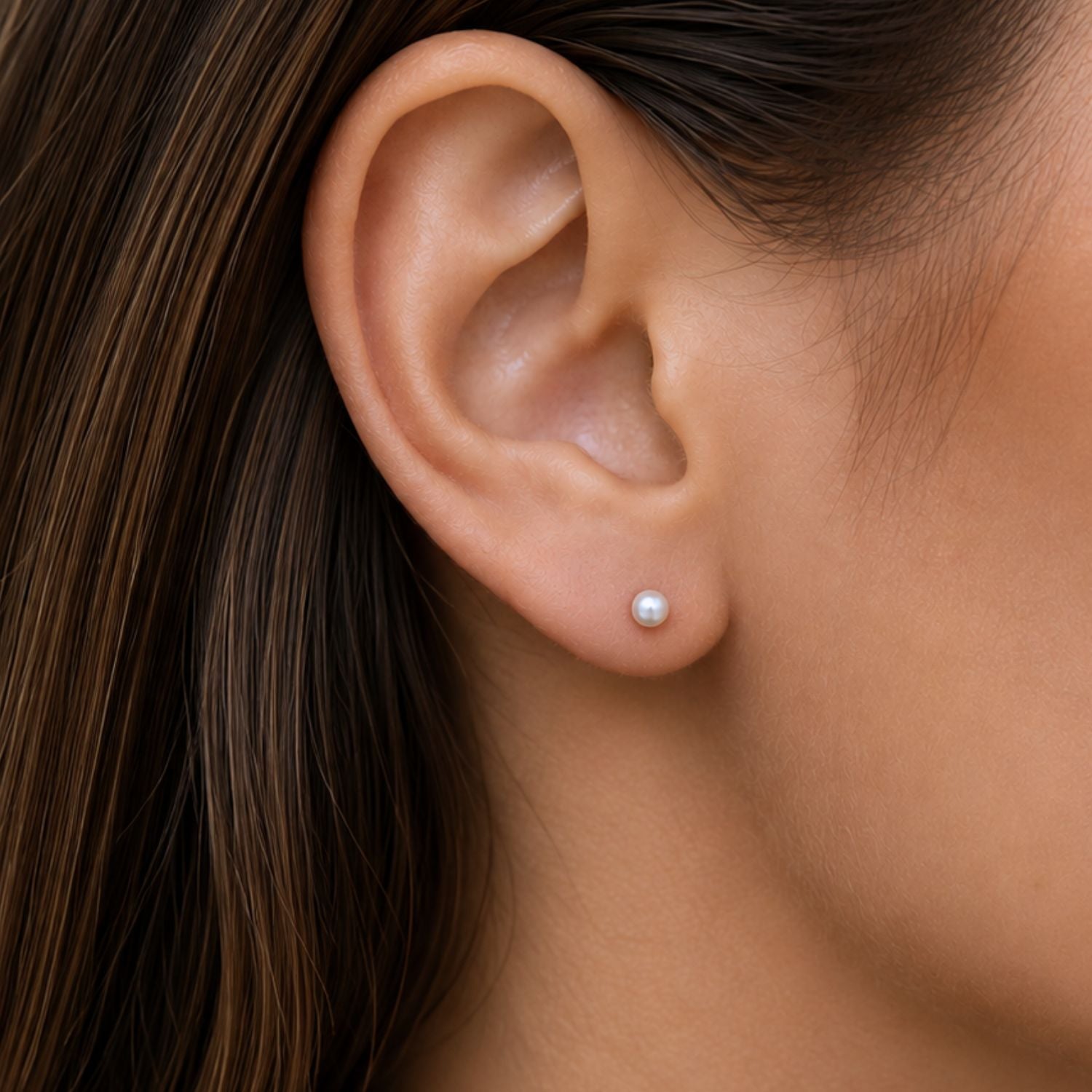 A close-up of a model's ear wearing a single small white pearl stud earring.