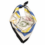 A silk scarf with a cream base, featuring blue and yellow stripes, a green fish illustration, and a black border, tied in a knot on a white background.
