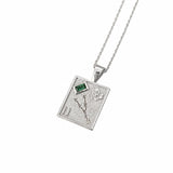 A silver-toned rectangular pendant necklace featuring a textured background with a small green rectangular gemstone, a flower motif, and the Roman numeral II, suspended from a fine silver chain against a white background.