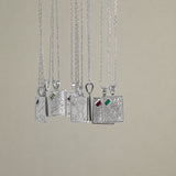 Eight silver pendant necklaces with detailed zodiac engravings and small colored gemstone accents, hanging against a solid beige background.