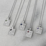 Five silver pendant necklaces with engraved zodiac constellations and small colored gemstone accents, arranged diagonally on a light gray marble surface.