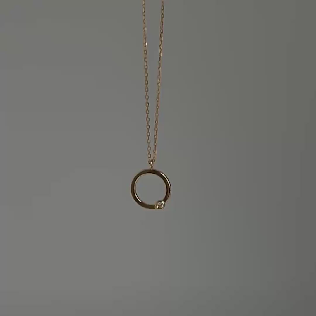 A gold chain necklace with a minimalist open circular pendant featuring a small lab-grown diamond on the right side, displayed on a clean gray background.