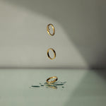 Three gold vermeil rings with lab grown diamonds set within a bezel, floating in the air on a green and grey background with water droplets.