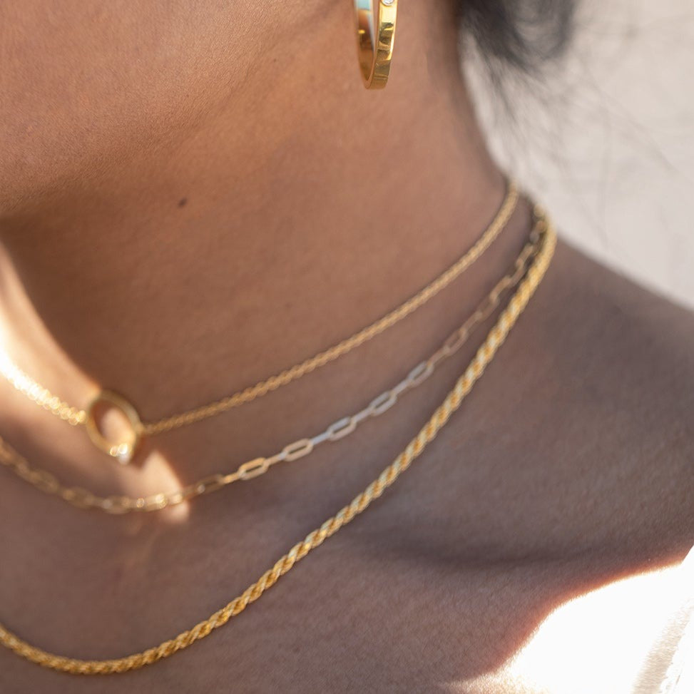 Three gold chain necklaces close up around a model's neck. 