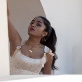 A model wearing gold jewelry framed with a white wall in front of her and archway in the background. She's wearing a pink satin dress. 