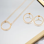 A 14K gold plated circular necklace on a mirror with gold hoop earrings.