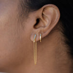 A pair of gold huggie hoop earrings with small lab-grown diamonds set along the front edge, close up on a model's ear with another gold dangle earring in the first piercing. 