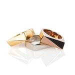 Three rectangular rings in gold, rose gold, and sterling silver stacked on a white background. 