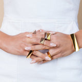 A person wearing multiple rings, including a gold-colored ring with a solid pattern and a silver ring, on a white background.