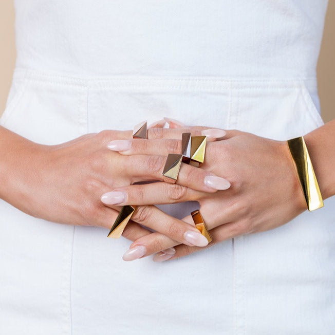 A person wearing multiple rings, including a gold-colored ring with a solid pattern and a silver ring, on a white background.