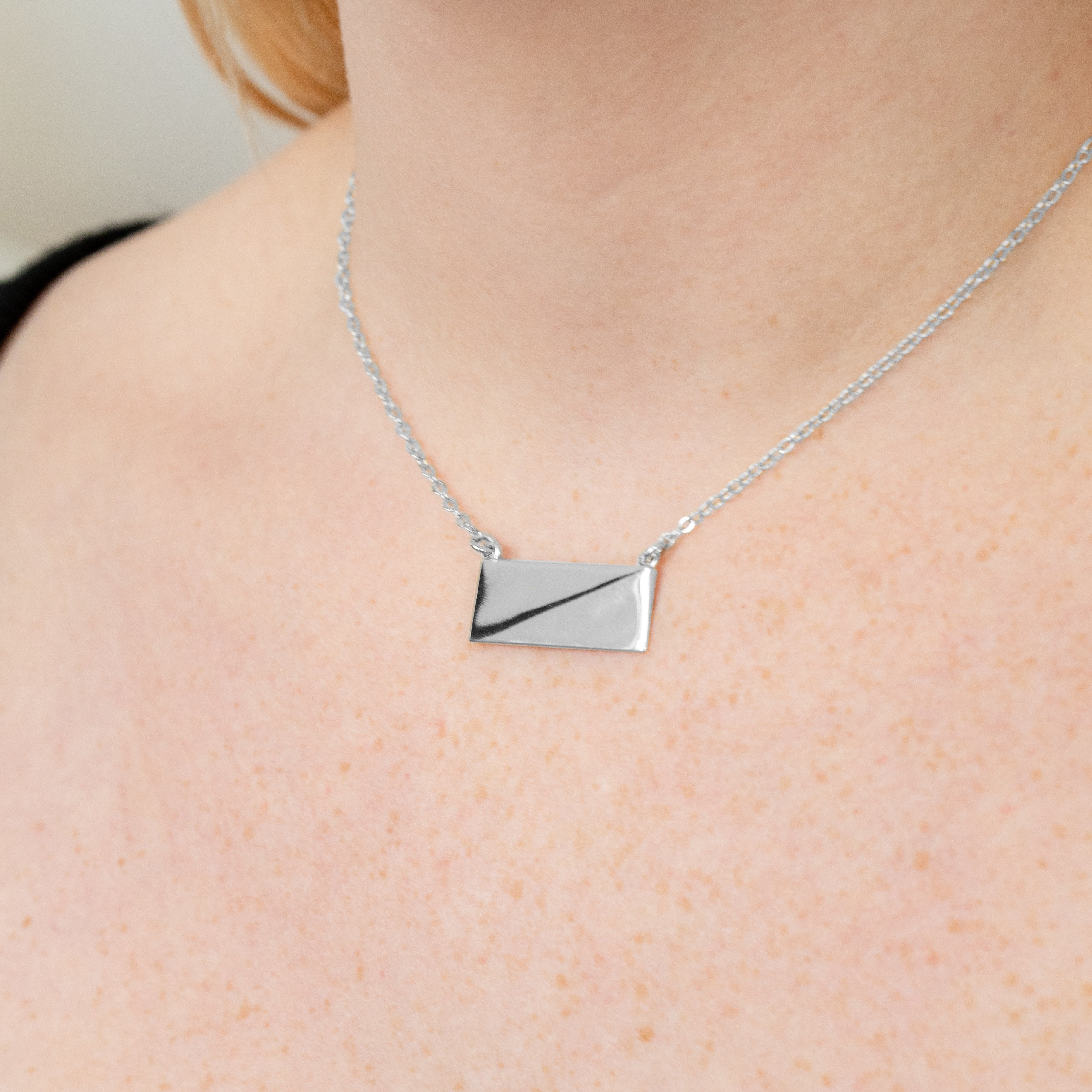 A sterling silver necklace pendant close up around a model's neck. 