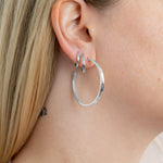 A pair of polished silver-tone open hoop earrings on a model's ear with two more smaller hoops in the second and third piercing. 